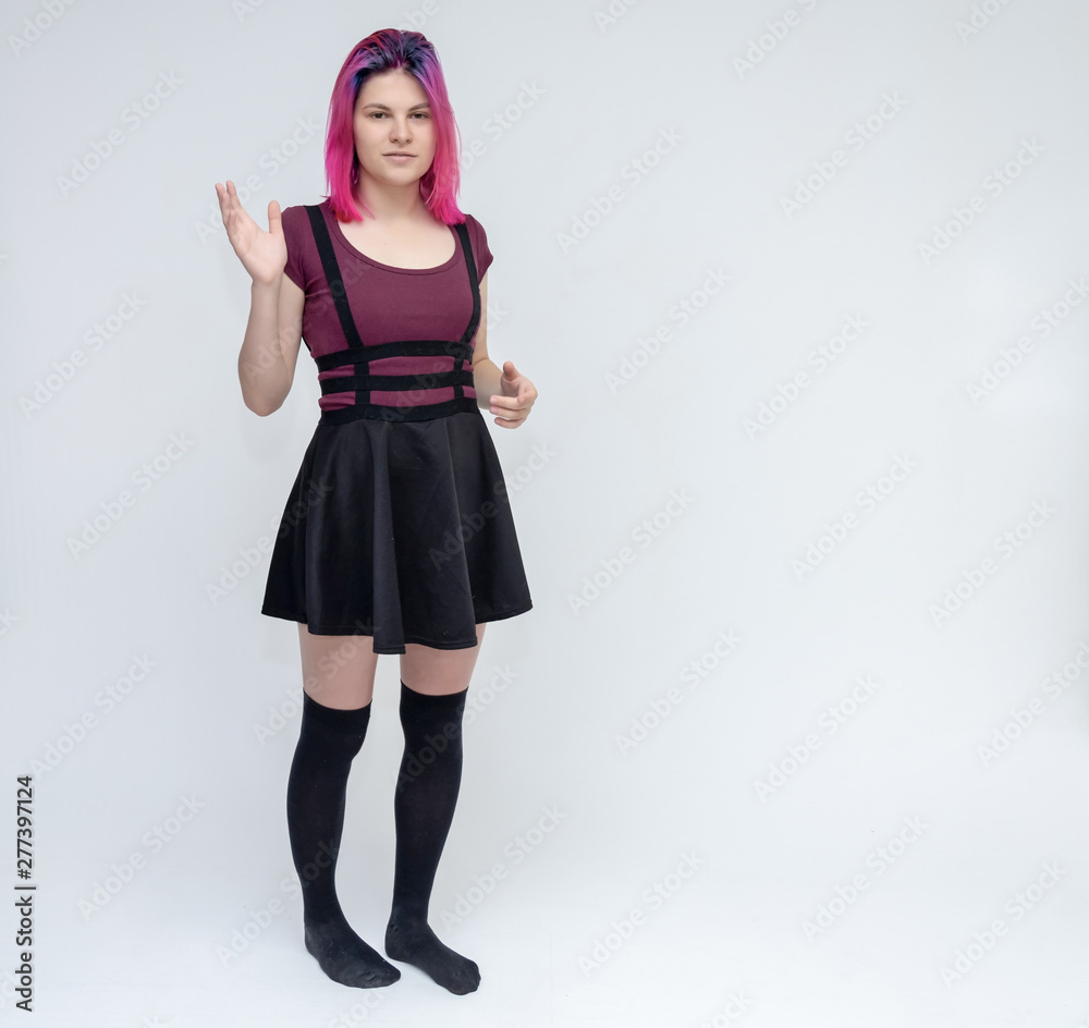 Full-length portrait of young pretty teenager girl in burgundy T-shirt and black dress with beautiful purple hair on a white background in the studio. Talking, smiling, showing hands with emotions. Full-length portrait of young pretty teenager girl in burgundy T-shirt and black dress with beautiful purple hair on a white background in the studio. Talking, smiling, showing hands with emotions.