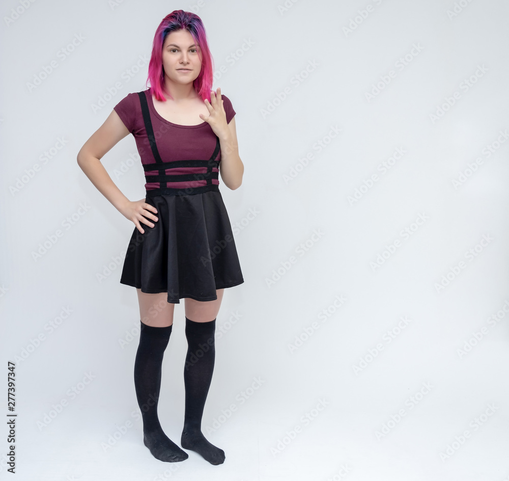 Full-length portrait of young pretty teenager girl in burgundy T-shirt and black dress with beautiful purple hair on a white background in the studio. Talking, smiling, showing hands with emotions. Full-length portrait of young pretty teenager girl in burgundy T-shirt and black dress with beautiful purple hair on a white background in the studio. Talking, smiling, showing hands with emotions.