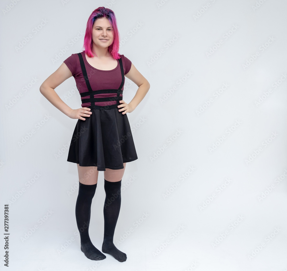Full-length portrait of young pretty teenager girl in burgundy T-shirt and black dress with beautiful purple hair on a white background in the studio. Talking, smiling, showing hands with emotions. Full-length portrait of young pretty teenager girl in burgundy T-shirt and black dress with beautiful purple hair on a white background in the studio. Talking, smiling, showing hands with emotions.