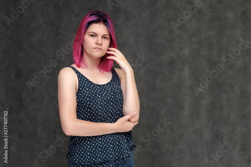 Portrait to the waist of a young pretty girl teenager in a T-shirt with beautiful purple hair on a gray background in the studio. Talking, smiling, showing hands with emotions.