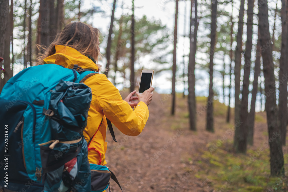 happy young beautiful woman with a hiking backpack phone in hand in a forest