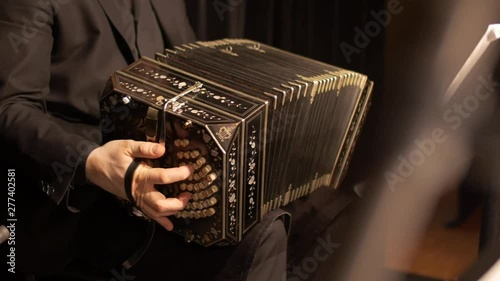 A Bandoneon accordion player is practicing for a tango music show, while a music stand is blurred in the foreground.