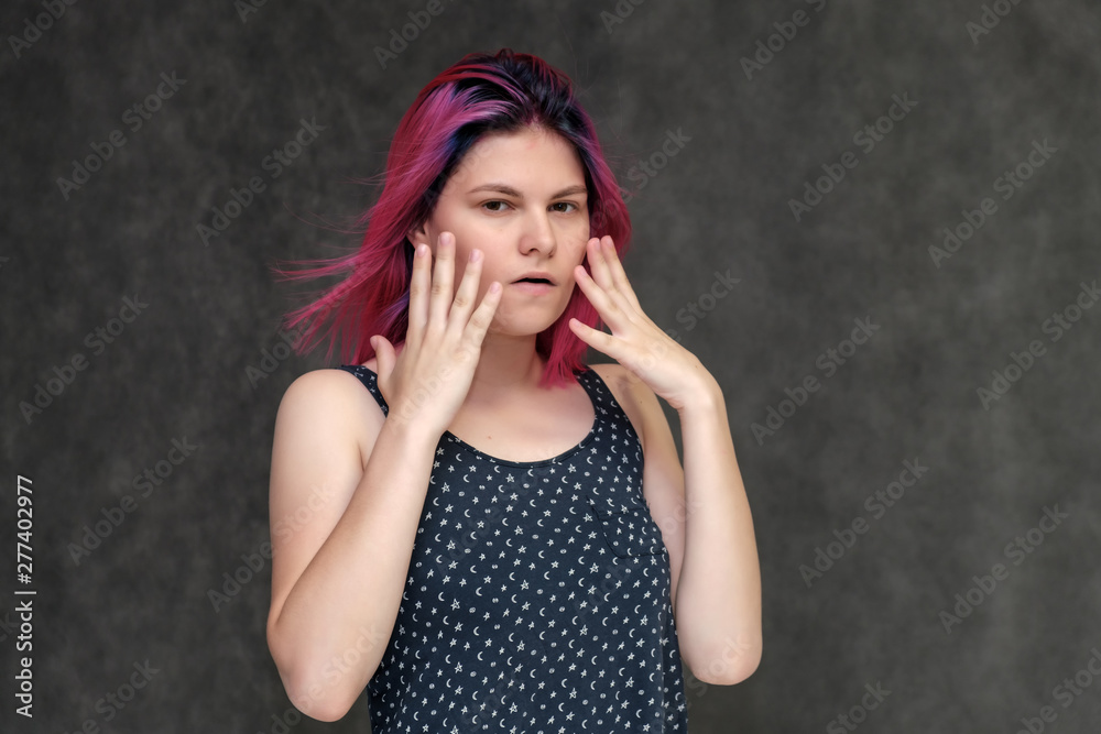 Portrait to the waist of a young pretty girl teenager in a T-shirt with beautiful purple hair on a gray background in the studio. Talking, smiling, showing hands with emotions. Portrait to the waist of a young pretty girl teenager in a T-shirt with beautiful purple hair on a gray background in the studio. Talking, smiling, showing hands with emotions.