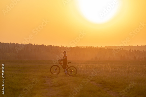 A girl rides a bicycle on the road against the backdrop of a bright sunset and yellow sun