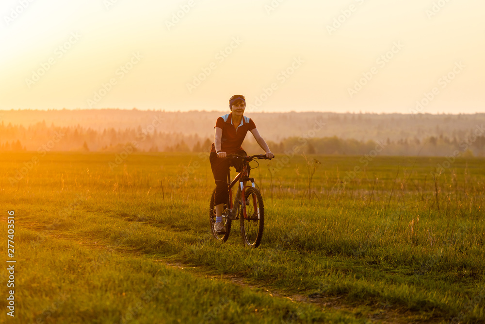 A girl rides a bicycle on the road against the backdrop of a bright sunset and yellow sun A girl rides a bicycle on the road against the backdrop of a bright sunset and yellow sun
