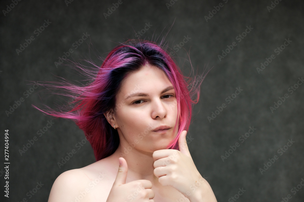 Obraz premium Close-up portrait of a young pretty teen girl with beautiful purple hair on a gray background in the studio. Smiles with emotions
