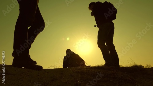 three travelers descend from hill in rays of sun one after other go beyond horizon. teamwork of business people. tourists travel with backpacks. business team is in hurry to win.