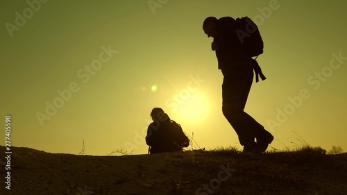 three travelers descend from hill in rays of sun one after other go beyond horizon. teamwork of business people. tourists travel with backpacks. business team is in hurry to win.