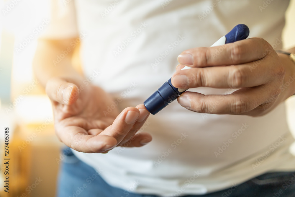 Fototapeta premium Close up of man hands using lancet on finger to check blood sugar level by Glucose meter. Use as Medicine, diabetes, glycemia, health care and people concept.