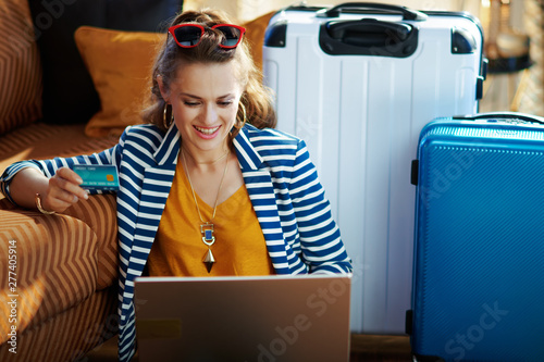 smiling trendy woman with credit card booking tickets on laptop