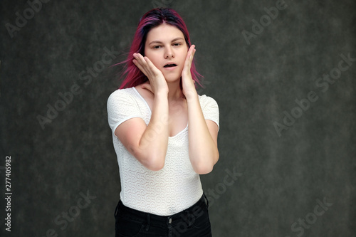 Portrait to waist of a young beautiful girl teenager in a white T-shirt with beautiful purple hair on a gray background in the studio. They say, they smile, they show hands with emotions. © Вячеслав Чичаев