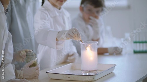 Children studying chemistry with practical experiments with a teacher. Close-up of a smart girl burning fire from a glask with chemical foam standing by table with shocked classmates. photo