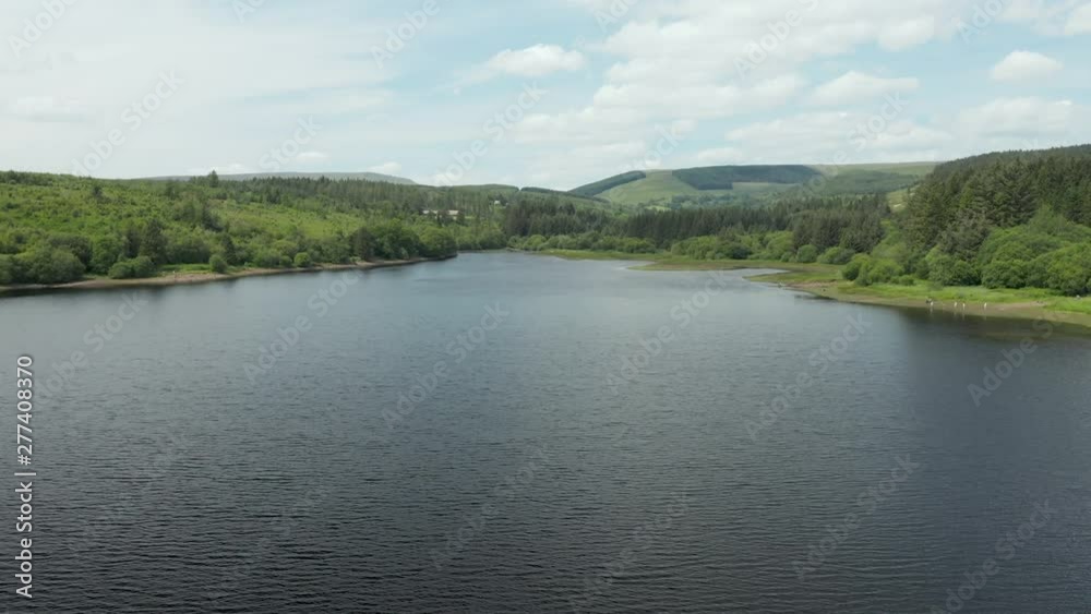 Aerial drone view flying over a reservoir surrounded by green hills and forest Aerial drone view flying over a reservoir surrounded by green hills and forest