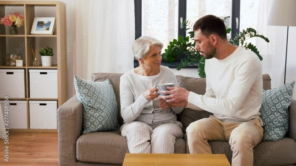 family, generation and people concept - happy smiling adult son bringing coffee to senior mother at home