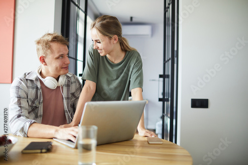Young couple interacting by table while man with headphones browsing in the net