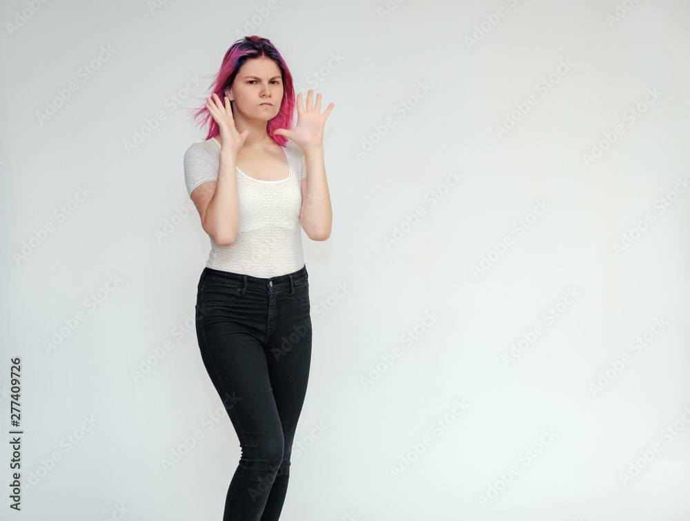 Portrait below the knee of a young beautiful girl teenager in a white T-shirt and black jeans with beautiful purple hair on a white background in the studio. They say, they smile, they show hands Portrait below the knee of a young beautiful girl teenager in a white T-shirt and black jeans with beautiful purple hair on a white background in the studio. They say, they smile, they show hands