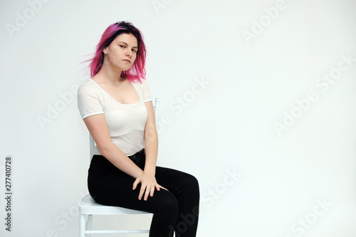 Portrait below the knee of a young beautiful girl teenager in a white T-shirt and black jeans with beautiful purple hair sitting on a white background in the studio. Says, shows hands with emotions.