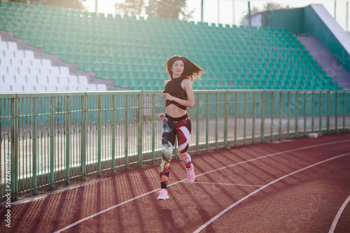 Obraz na płótnie Sport. Athletic young brunette woman in pink sneakers, leggings and top run on running track stadium at sunset. her hair is developing. Concept run. concept of a healthy lifestyle. w salonie