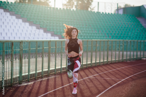 Obraz na płótnie Sport. Athletic young brunette woman in pink sneakers, leggings and top run on running track stadium at sunset. her hair is developing. Concept run. concept of a healthy lifestyle. w salonie