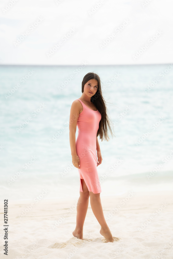 The brunette in a pink fitting dress walks on a snow-white beach The brunette in a pink fitting dress walks on a snow-white beach