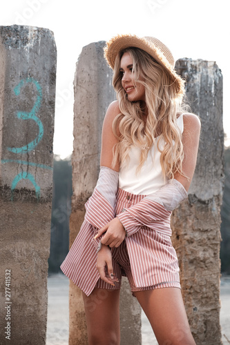 Beautiful, fashionable and natural smiling young woman with long loose blonde hair in a straw hat. Countryside landscape, stones at the background. Summertime, summer outdoor photoshoot on the shore 