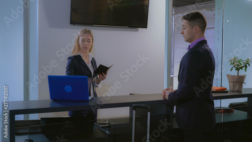 visitor giving passport to receptionist in hotel. Beautiful caucasian worker entering information on computer check booking. Businessman with suitcase standing near reception desk. Mixed race man