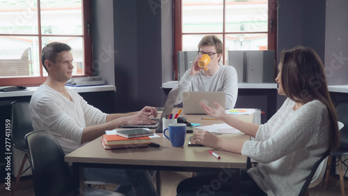 Brainstorming in the contemporary office. Young professional people talking using computer paper documents dressed in casual clothes. Two handsome man and caucasian woman discussing project.