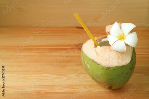 Fresh young coconut water in coconut shell with Plumeria flower on wooden table 