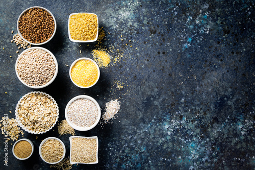 Selection of whole grains in white bowls - rice, oats, buckwheat, bulgur, porridge, barley, quinoa, amaranth on dark background