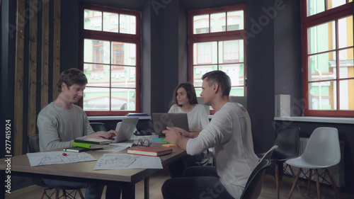 Morning in startup company office. Professional caucasian guy greets with friends colleagues. shakes hands with a man and kiss on the cheek woman. Businesswoman and businessman sitting at the working