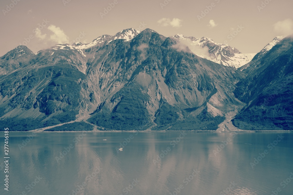 Black and white vintage filter view of Alaska coast line meeting rugged snowy mountain peaks