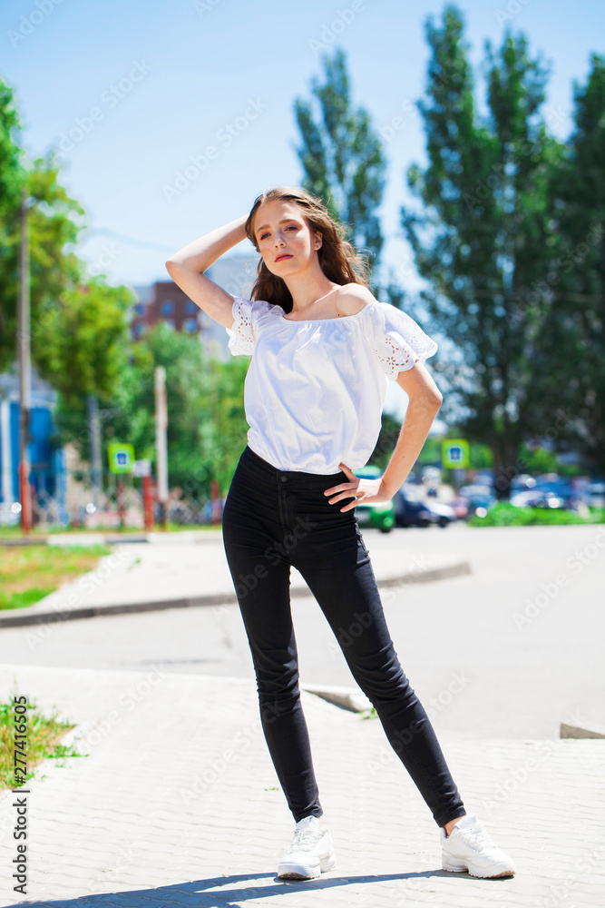 Young beautiful brunette woman in jeans and white blouse walking in summer street Young beautiful brunette woman in jeans and white blouse walking in summer street