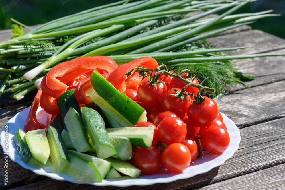 Fresh vegetables and greenery on a wooden background outdoors.