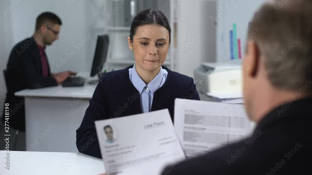 Female job candidate nervously waiting HR manager looking through resume Female job candidate nervously waiting HR manager looking through resume
