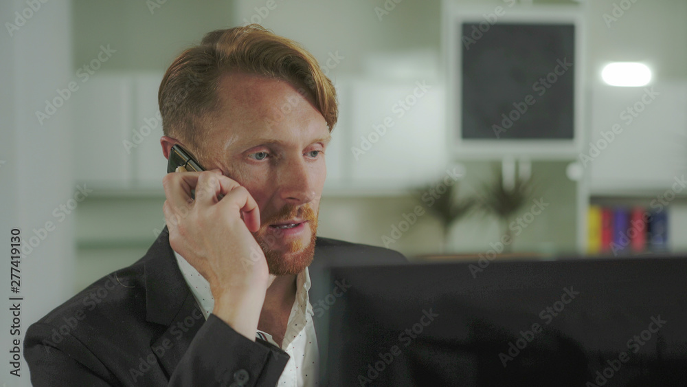 Red-haired man sitting at a computer and calling on the phone. UHD Red-haired man sitting at a computer and calling on the phone. UHD