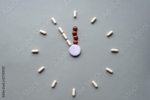 Clock created from white pills and brown tablets on green background. Right time for using medicines. Brown and white pills, tablets and capsules is five to twelve. Concept: medicine, drugs, healthcar photo