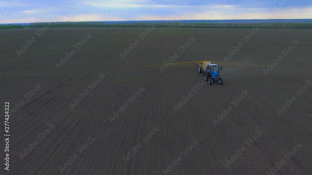 A tractor is driving along the field, which processes the field, the camera is moving toward the tractor, shooting from the air.