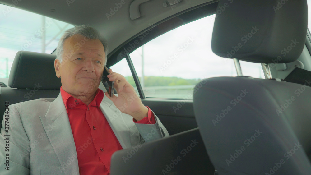 elegant male has phone conversation. Middle aged man talking on the smartphone in car wearing in red shirt and formal suit. elegant male has phone conversation. Middle aged man talking on the smartphone in car wearing in red shirt and formal suit.