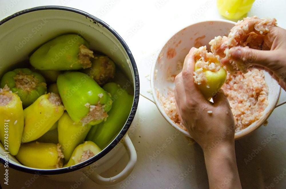 Obraz premium stuffed peppers in the cooking process on a white plate with hands, minced meat with rice and white saucepan