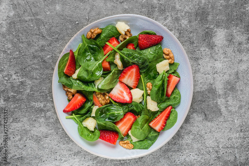 salad with strawberry, spinach leaves, parmesan cheese and walnuts on concrete background. healthy diet food