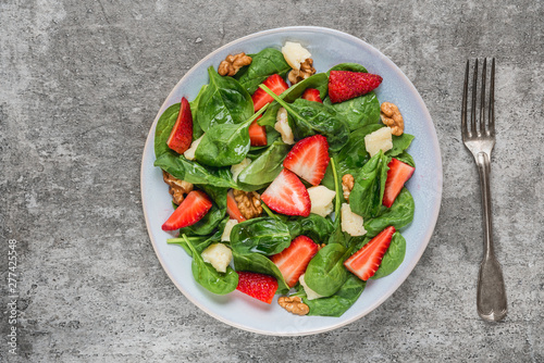 Fresh strawberry salad with spinach leaves, parmesan cheese and walnuts with fork. healthy keto diet food