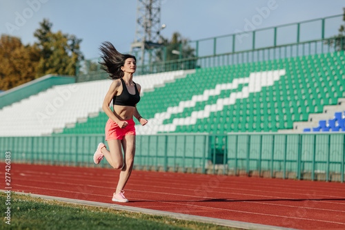 Obraz na płótnie Young fitness brunette woman in shorts and top running on a stadium track. Athlete girl doing exercises on the training at stadium. Healthy active lifestyle. w salonie