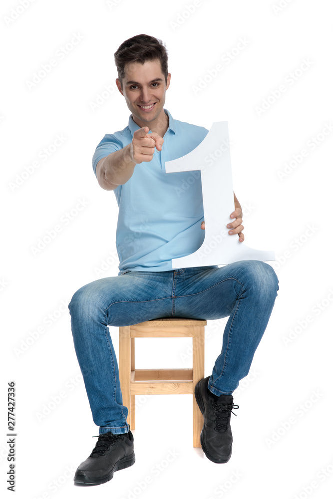 Positive casual guy pointing and holding a number one