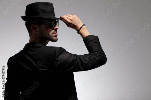 Rear view of a mysterious casual man adjusting his cap