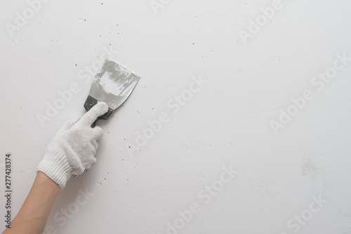 Working tool, spatula in hand against the background of a white wall, work plasterer. Putty walls with their own hands.