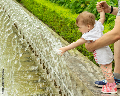 Baby pink sandals playing with water. The baby touches the water in the fountain, shoves hands under jets of water. Girl in the fountain photo