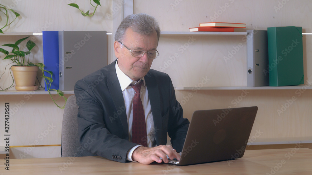 Portrait aged man straightening tie. Businessman sitting in the office working on computer. Portrait aged man straightening tie. Businessman sitting in the office working on computer.