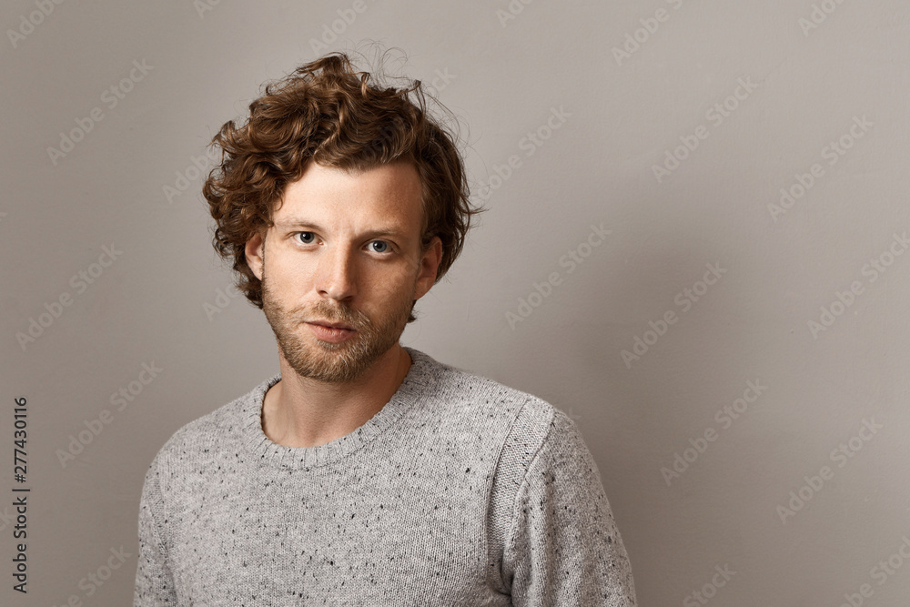 Fototapeta premium Masculine beauty, style and fashion concept. Fashionable 25 year old hipster guy with stubble and blue eyes posing isolated against copyspace wall background, wearing stylish knitted sweater