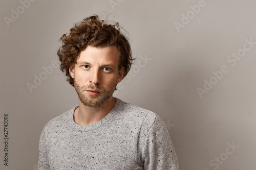 Masculine beauty, style and fashion concept. Fashionable 25 year old hipster guy with stubble and blue eyes posing isolated against copyspace wall background, wearing stylish knitted sweater