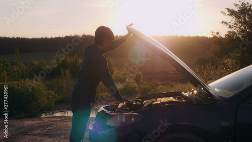 Fotografie Woman mechanic opening car hood roadside in village